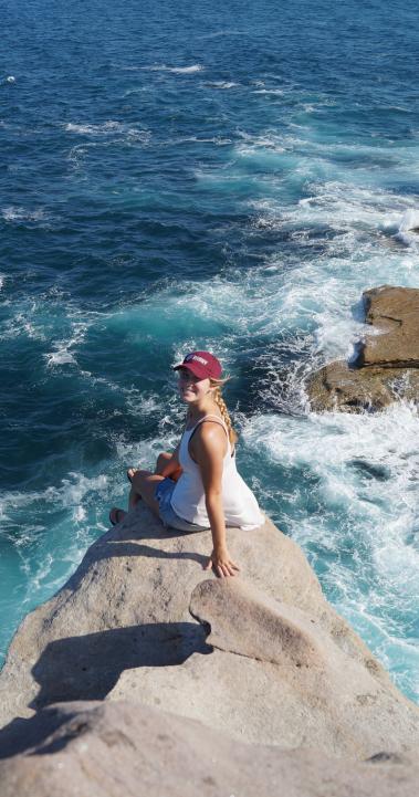 a student poses for a photo on a seaside rock in Sydney
