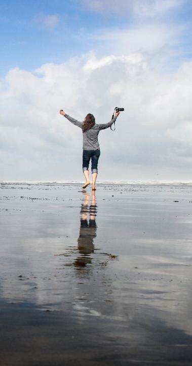 a student holding a DSLR camera in the air while walking on 90 Mile Beach in New Zealand