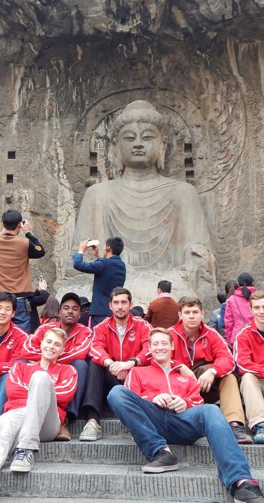 engineering students sitting on the steps in front of a stone carving of buddha