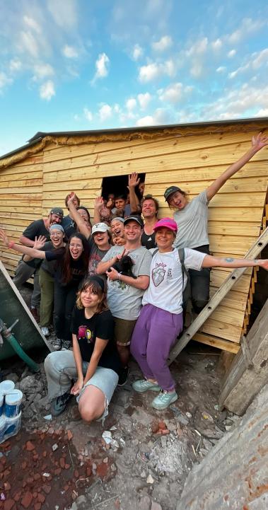a group of students pose for a photo with a transitional home they built for a family in need