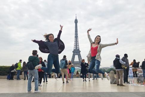 two students jump into a pose for a photo at the Eiffel Tower