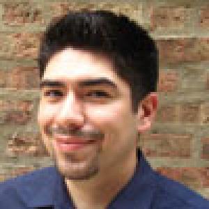 Smiling person with short dark hair and a goatee, in front of a brick wall. This alt text was added with Al; accuracy may vary.