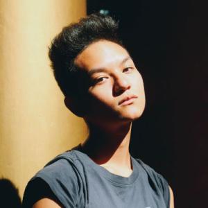 Young person in shadow with contemplative expression, sunlight on face. This alt text was added with Al; accuracy may vary.