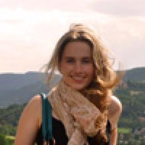 Person with brown hair and red lipstick outdoors, sunlight on face. This alt text was added with Al; accuracy may vary.