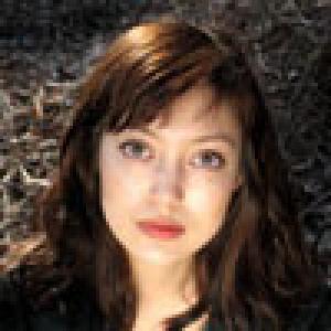 A person with brown hair and an expressionless face outdoors. This alt text was added with Al; accuracy may vary.