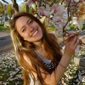 Smiling person near flowering tree in spring. This alt text was added with Al; accuracy may vary.