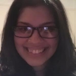 Smiling woman indoors with long hair and glasses. This alt text was added with Al; accuracy may vary.