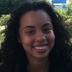 Smiling woman outside, green background. This alt text was added with Al; accuracy may vary.