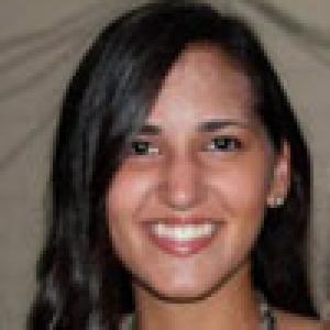 Person in a beanie and jacket smiles outdoors in autumn setting. This alt text was added with Al; accuracy may vary.