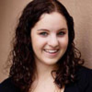 Smiling person with curly hair against a brown background. This alt text was added with Al; accuracy may vary.