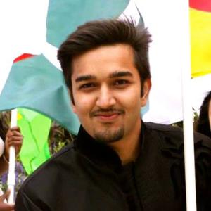 Smiling man holding flags, wearing a black jacket. This alt text was added with Al; accuracy may vary.