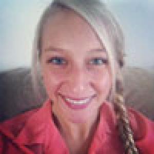 Smiling person with blonde hair braided, wearing a red shirt. This alt text was added with Al; accuracy may vary.