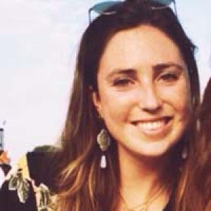 Photograph of a smiling woman outdoors with long brown hair and sunglasses on her head. This alt text was added with Al; accuracy may vary.