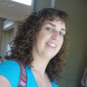 Curly-haired person smiling, wearing a blue shirt indoors. This alt text was added with Al; accuracy may vary.