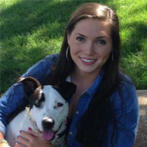 Young woman smiling with a black and white dog outdoors on sunny day. This alt text was added with Al; accuracy may vary.