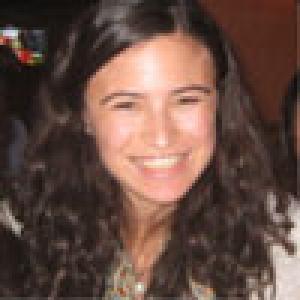 Riverside scene with trees, people, and a church tower under a clear blue sky. This alt text was added with Al; accuracy may vary.