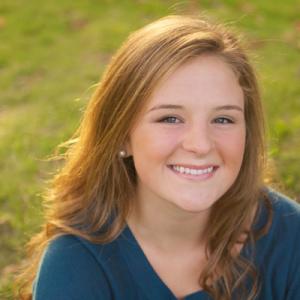 Outdoor portrait, smiling young woman in a park. This alt text was added with Al; accuracy may vary.