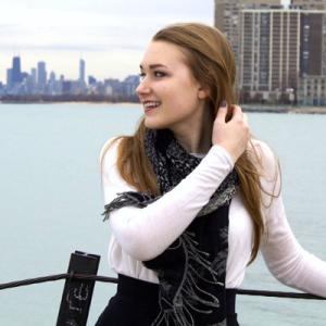 Young woman smiling, wearing a striped shirt, with greenery and water in the background. This alt text was added with Al; accuracy may vary.