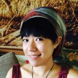 Person smiling, wearing a headscarf, seated indoors, warm tones in the background. This alt text was added with Al; accuracy may vary.