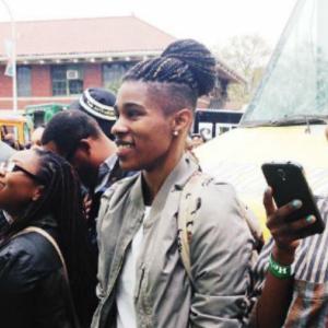 Group of people smiling and taking photos, one person in focus with braided hair. This alt text was added with Al; accuracy may vary.