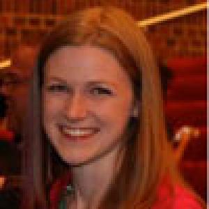 Smiling person with long brown hair, green blurred background. This alt text was added with Al; accuracy may vary.