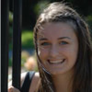 Smiling woman with long brown hair beside a fence in a garden setting. This alt text was added with Al; accuracy may vary.