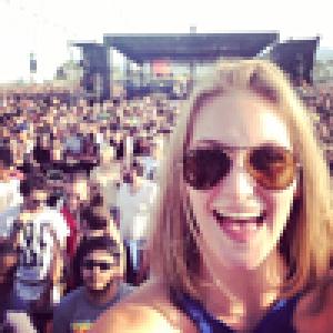Smiling woman wearing sunglasses with a large crowd behind her. This alt text was added with Al; accuracy may vary.