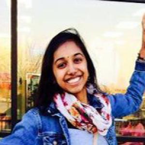 Smiling person in front of a glass window, wearing a denim jacket and floral scarf. This alt text was added with Al; accuracy may vary.