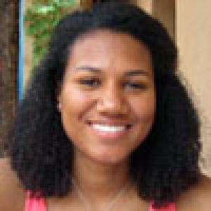 Smiling person with curly hair and a pink top. This alt text was added with Al; accuracy may vary.