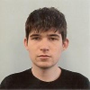 Young person with short dark hair and a neutral expression, wearing a black shirt. This alt text was added with Al; accuracy may vary.