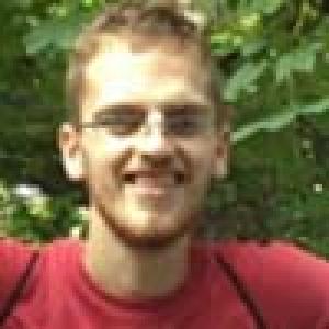 Smiling person wearing glasses, outdoors with greenery. This alt text was added with Al; accuracy may vary.