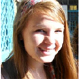 Smiling person with short hair, wearing a pink shirt against a blurred background. This alt text was added with Al; accuracy may vary.