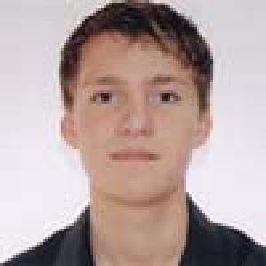 Young person with short hair and neutral expression, wearing a dark shirt. This alt text was added with Al; accuracy may vary.