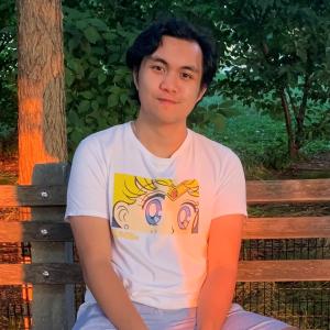 Avery Trinidad sitting on a bench outside in front of some trees. 