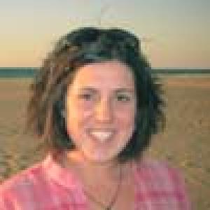 A person in a blue jacket salutes with an indoor background. This alt text was added with Al; accuracy may vary.