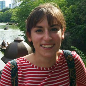 Smiling person in a striped shirt, outdoors with trees and a lake in the background. This alt text was added with Al; accuracy may vary.