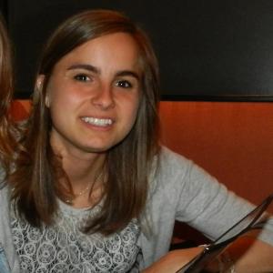 Smiling person with long hair, wearing a gray sweater, sitting indoors. This alt text was added with Al; accuracy may vary.