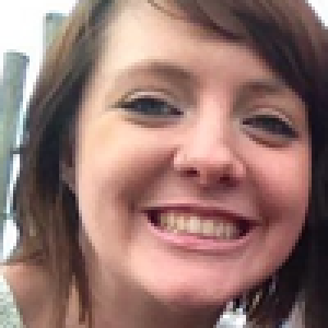 Woman with curly hair smiling indoors, wearing a blue top. This alt text was added with Al; accuracy may vary.