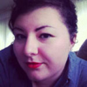 Smiling person with curly hair against a beige background. This alt text was added with Al; accuracy may vary.