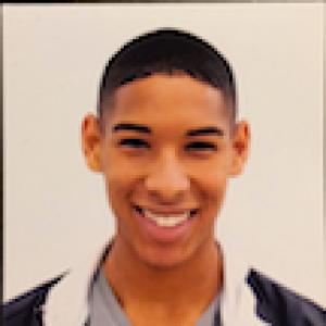 Smiling person in a black and white jacket against a plain background. This alt text was added with Al; accuracy may vary.