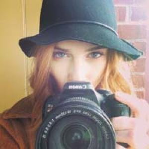 1. Woman smiling, seated outdoors on a wooden chair.
2. Woman in hat holding camera, looking directly. This alt text was added with Al; accuracy may vary.