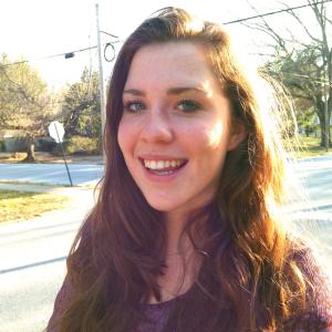 Smiling woman with long hair outdoors, wearing a purple sweater. This alt text was added with Al; accuracy may vary.