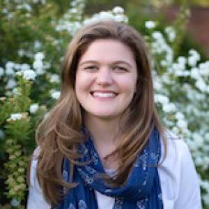 Smiling woman with long hair in a library. This alt text was added with Al; accuracy may vary.