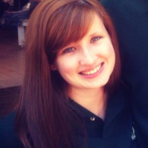 Young man with glasses, wearing a plaid shirt, smiling against a plain background. This alt text was added with Al; accuracy may vary.