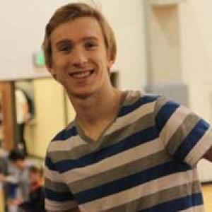 Young person smiling in a striped shirt indoors. This alt text was added with Al; accuracy may vary.