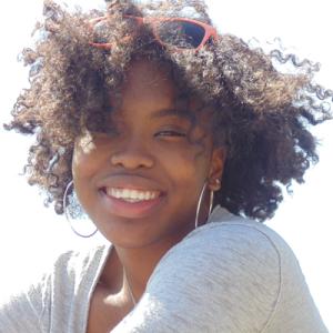 Smiling woman with long hair, beside a lamp in a stone-walled room. This alt text was added with Al; accuracy may vary.