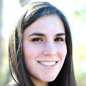 Young person with dark, curly hair wearing a polka dot shirt, neutral expression. This alt text was added with Al; accuracy may vary.