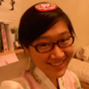 Smiling person wearing glasses and traditional clothing indoors. This alt text was added with Al; accuracy may vary.