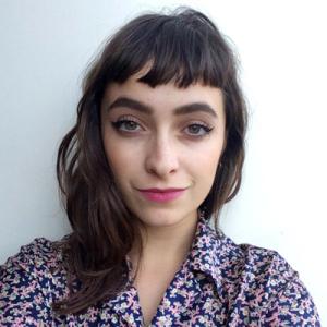Smiling woman in a red striped shirt outdoors with greenery and a pond. This alt text was added with Al; accuracy may vary.