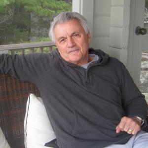 John Irving, sitting on a couch outdoors. There are trees in the background.